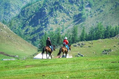 Rear view of people riding horses on field