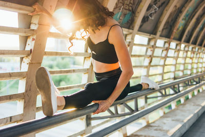 Full length of female athlete doing split on railing of footbridge against bright sun