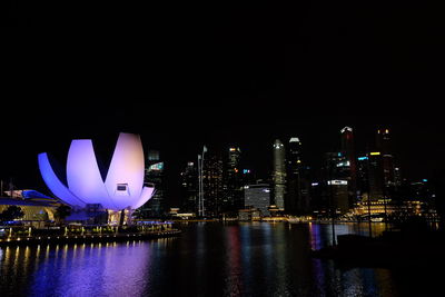 Illuminated city by river against sky at night