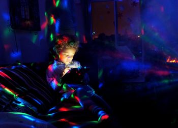 Boy using digital tablet while sitting at illuminated bedroom