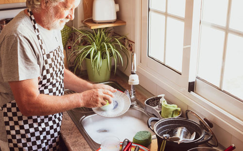 Senior man cleaning plate in kitchen at home