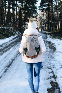 Rear view of woman carrying backpack while walking on snow covered road