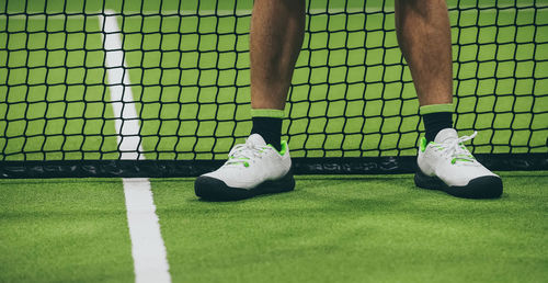 Closeup view of male legs with shorts in a padel tennis court standing near the net. foot on green