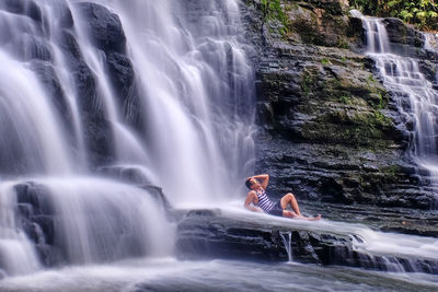 Side view of man sitting in waterfall