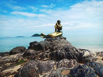 Statue on rock by sea against sky