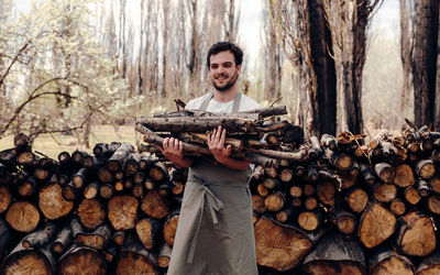 Portrait of young man standing on logs in forest