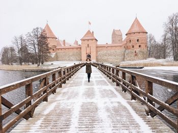 Rear view of man standing on bridge against sky during winter