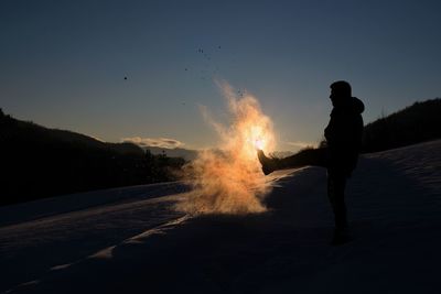 Silhouette man standing by bonfire against sky at night