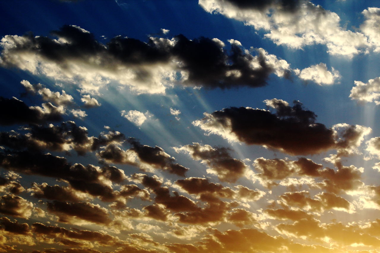 LOW ANGLE VIEW OF SUN STREAMING THROUGH CLOUDS DURING SUNSET