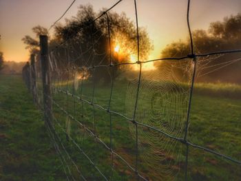 Fence on field against sky during sunset