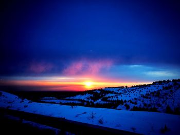 Snow covered land against sky during sunset