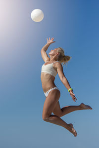 Low angle view of woman jumping against clear blue sky