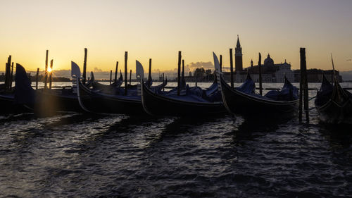 Boats moored in canal at sunset