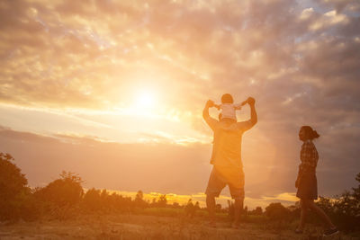 People standing on field against sky during sunset