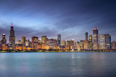 Illuminated buildings in city against sky at dusk