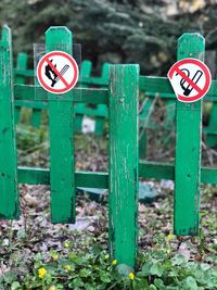 Warning signs on green wooden fence at field