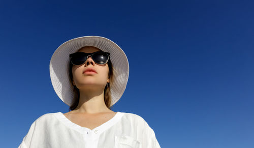 Low angle view of woman wearing sunglasses against clear blue sky