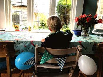 Rear view of boy sitting on table at home