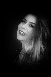 Close-up portrait of a smiling young woman over black background