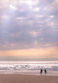 People walking at beach against sky during sunset