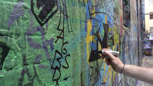 Cropped image of person drawing on graffiti wall