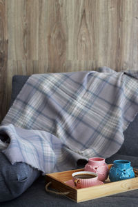 Coffee cup by fabric in serving tray on sofa at home