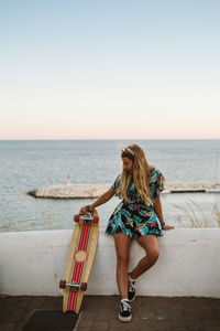 Young female with long board skate in front of the mediterranean sea