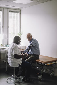 Mature doctor checking blood pressure of senior male patient sitting in clinic