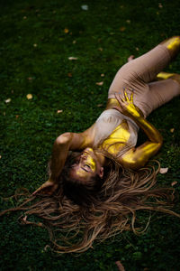 High angle view of woman lying on grass , her body is completely covered with glitter