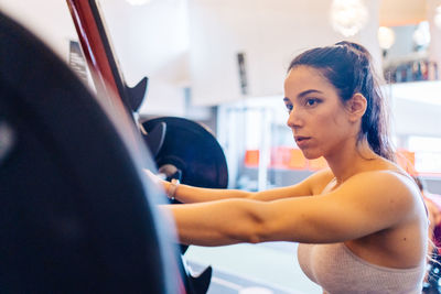 Side view portrait of young woman exercising in gym lifting 