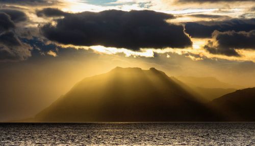 Sunlight streaming through clouds over sea during sunset