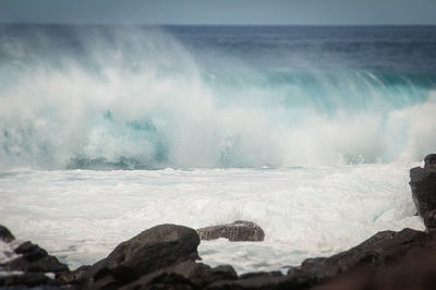 Waves breaking on rocks against sky