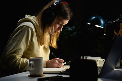 Woman listening music in headphones and using laptop at night