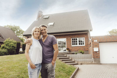 Portrait of smiling mature couple standing in front of their home