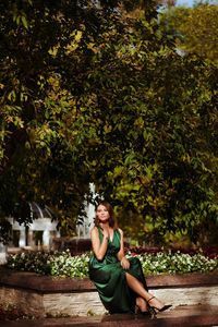 Portrait of sexy woman sitting in autumn park wearing silk green dress 