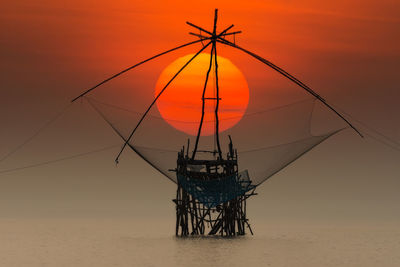 Silhouette electricity pylon on beach against sky during sunset