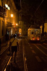 Illuminated railroad tracks on street in city at night