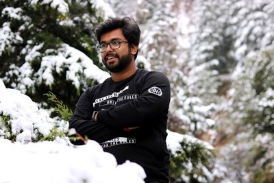 Smiling young man with arms crossed standing against mountain during winter