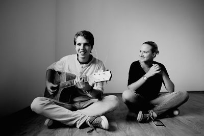 Smiling young man playing guitar by friend on hardwood floor at home