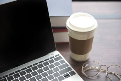 Close-up of laptop with disposable cup and eyeglasses on table