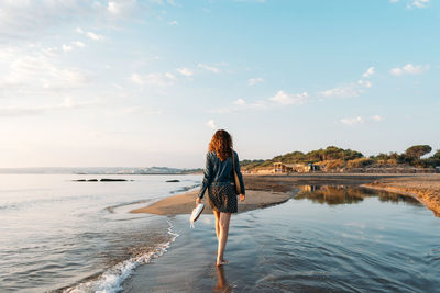 Rear view of woman standing at beach against sky