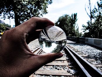 Close-up of hand holding railroad track against sky