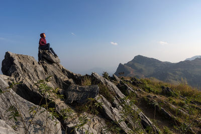 Low angle view of woman sitting on rocks against sky