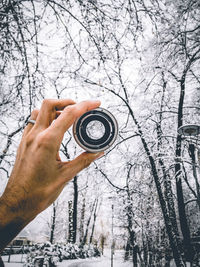 Cropped hand holding lens against bare trees