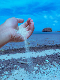 Cropped hand playing with sand at beach against sky