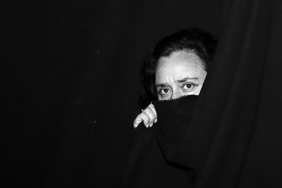 Close-up portrait of woman covering face with fabric against black background
