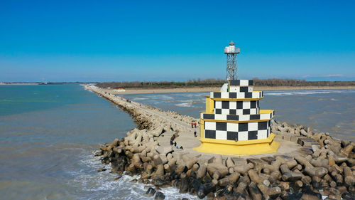 Lighthouse by sea against clear blue sky