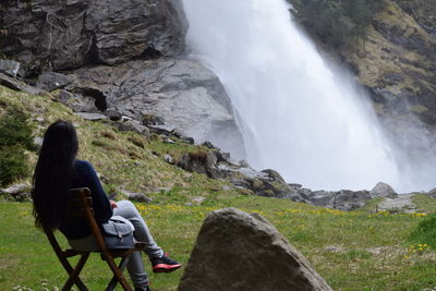 Rear view of woman sitting on chair while looking at waterfall