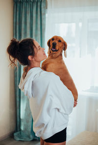 Side view of woman holding dog at home