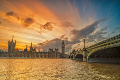 Westminster bridge over thames river by big ben and houses of parliament against sky during sunset